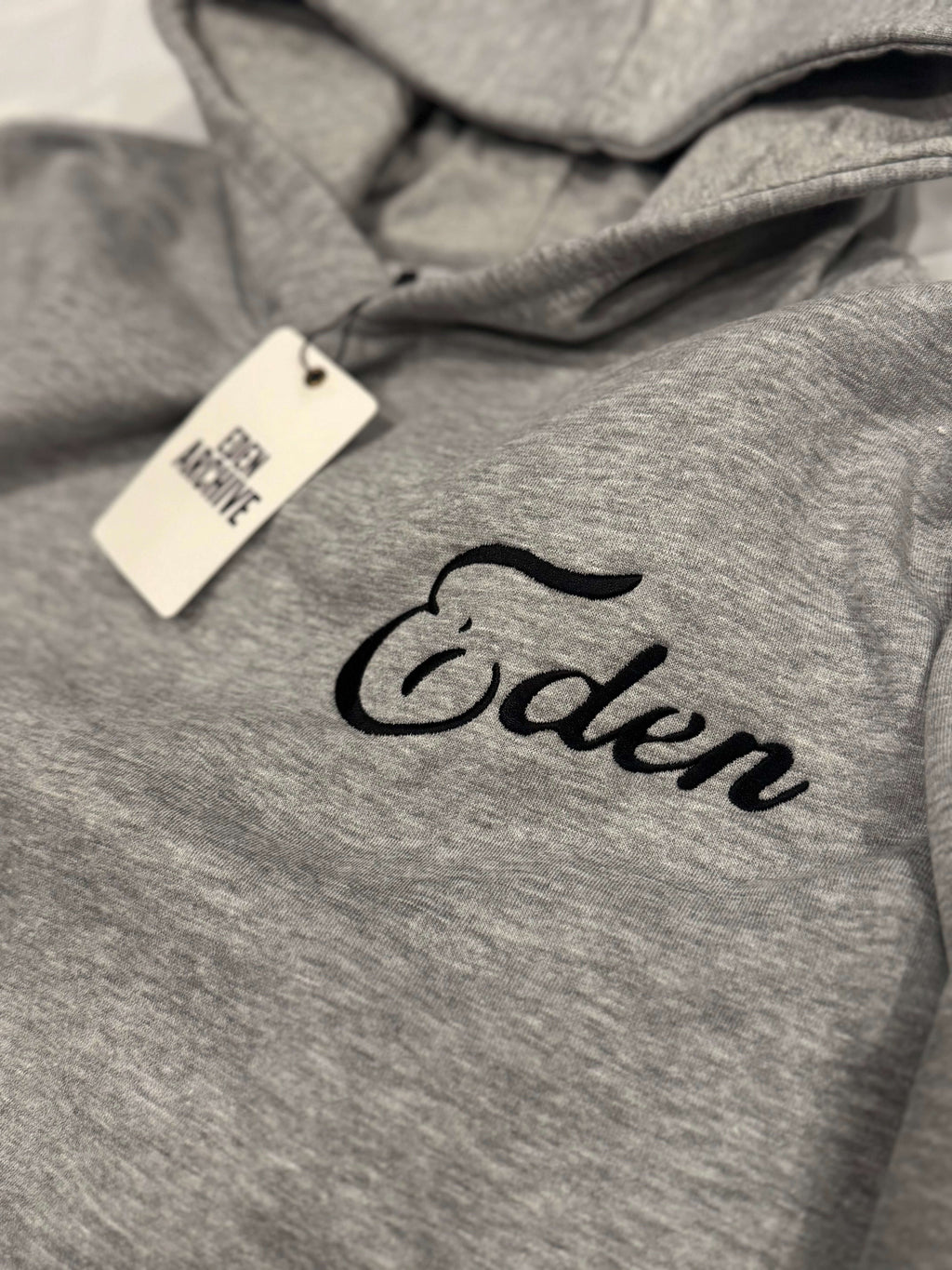 Close-up of the EDEN RHINESTONE SWEATSUIT hoodie showcasing the 'Eden' logo on a grey background.