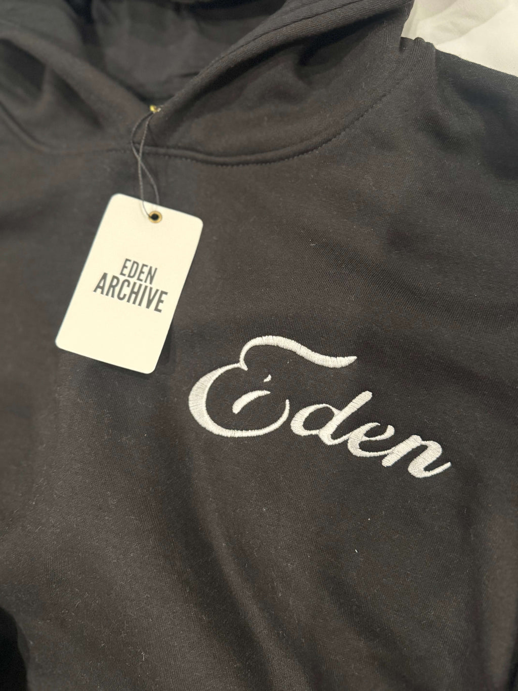 Close-up of EDEN RHINESTONE SWEATSUIT hoodie showing 'Eden' embroidery and tag.